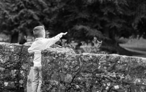 Mel Hudson Family Photography Belfast, black & white image of boy standing at a stone bridge throwing sticks into the water